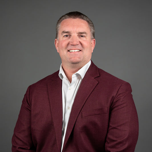 Man wearing a maroon blazer over a white shirt against a gray background