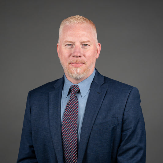 Man wearing a blue suit and striped tie against a gray background