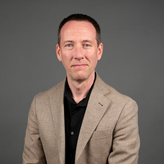 Man wearing a beige blazer over a black shirt against a gray background