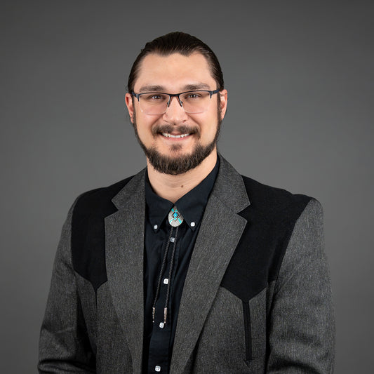 Man wearing glasses and a gray blazer with a dark shirt against a gray background