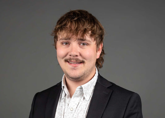 Man wearing a black blazer over a light shirt against a gray background