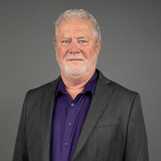 Man wearing a gray suit and purple shirt against a gray background