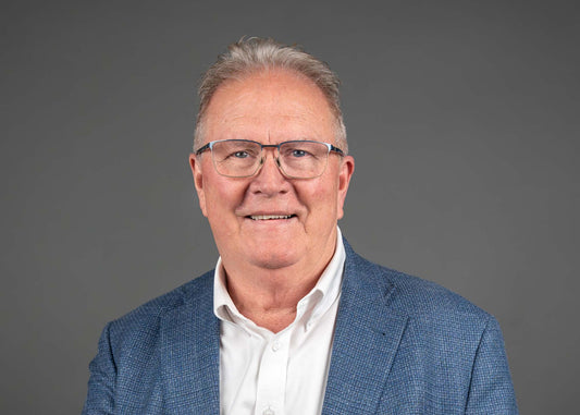 Man wearing glasses and a blue blazer against a gray background