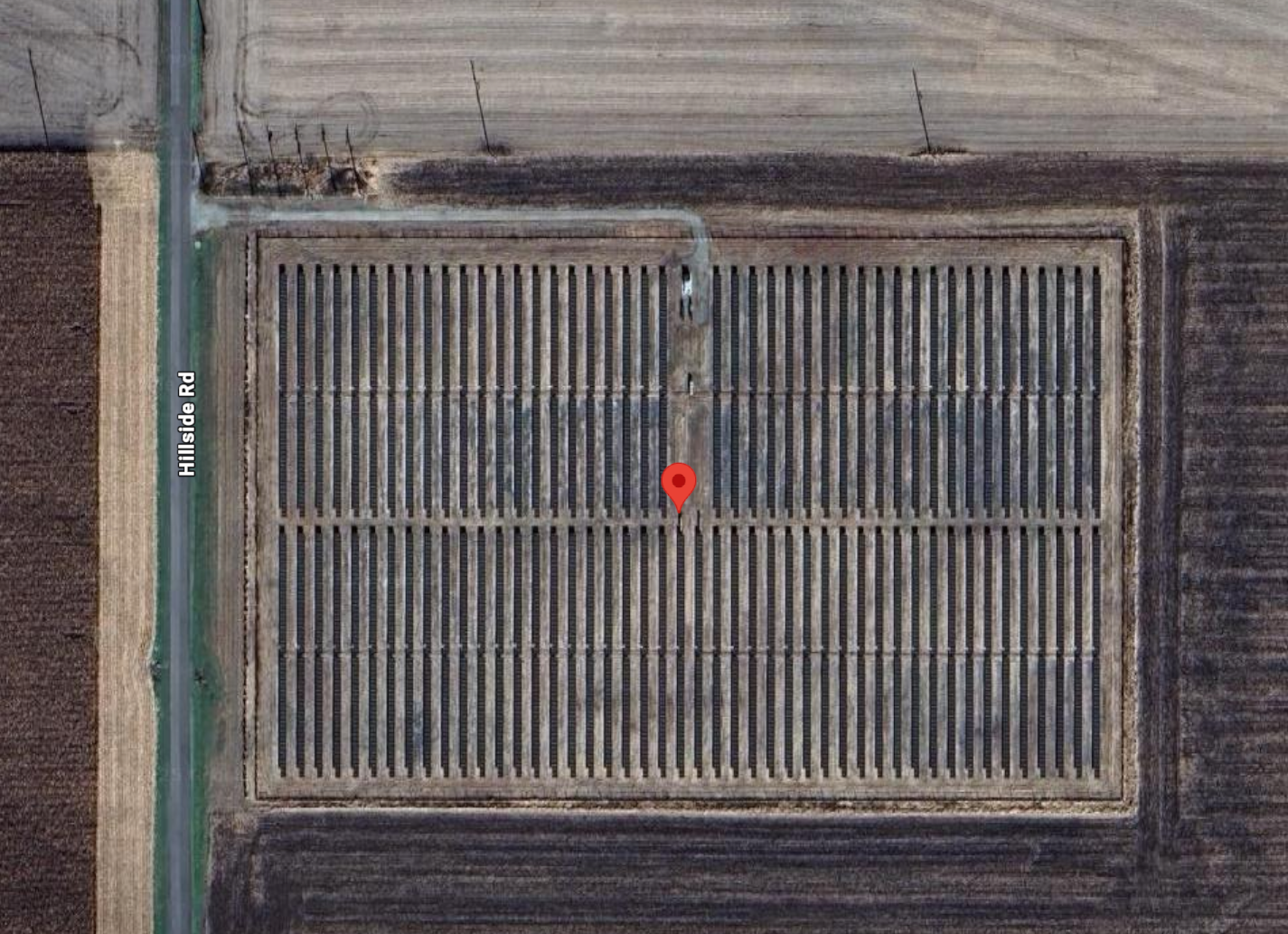 Aerial view of a large rectangular solar farm with a red location pin on a field.