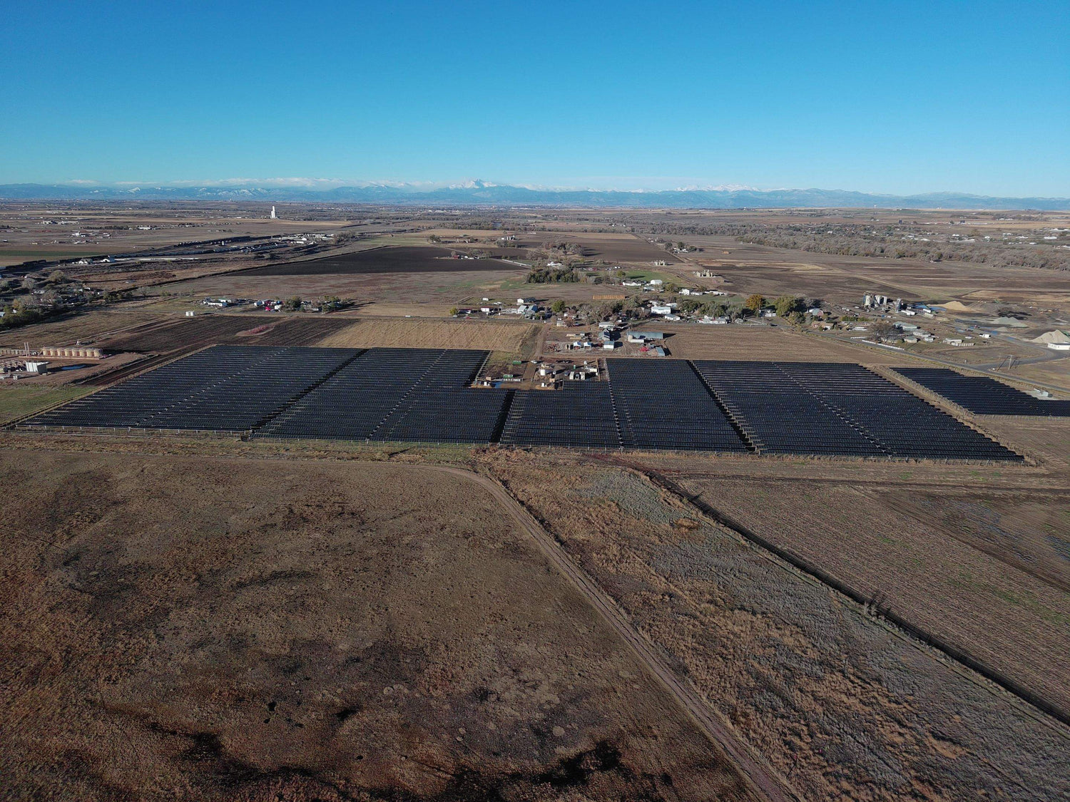 Aerial view of a large solar farm in a rural landscape with mountains in the distance.