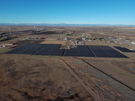Aerial view of a large solar farm in a rural landscape with mountains in the distance.