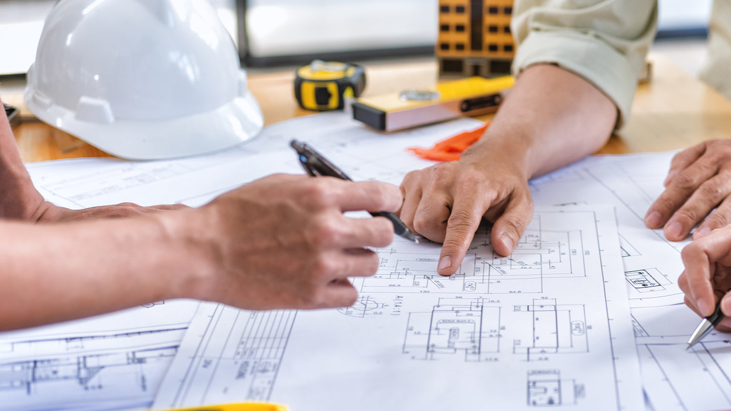 Two people reviewing blueprints with construction tools on a table