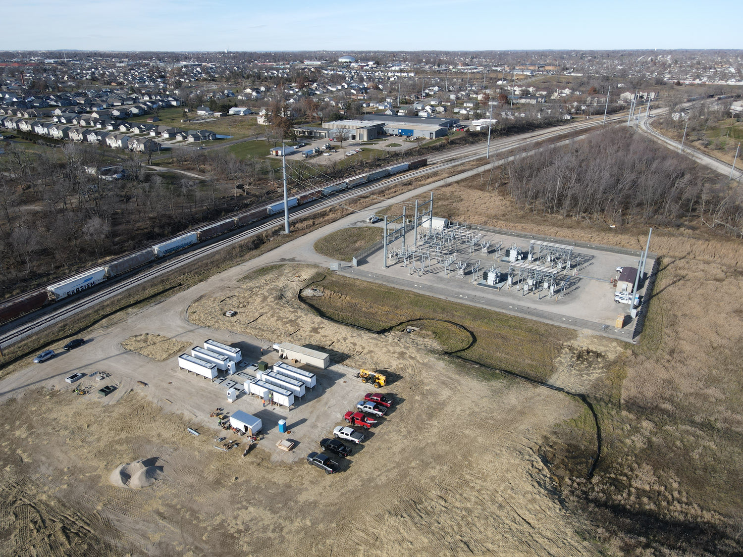 Aerial view of a BESS site with equipment and vehicles near a road and train tracks.