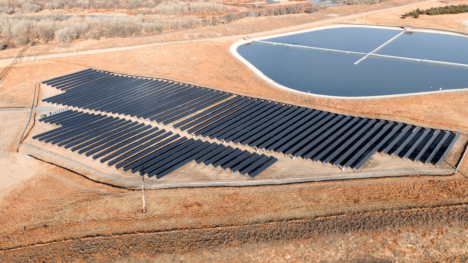 Solar panels installed on a flat field with a water body in the background