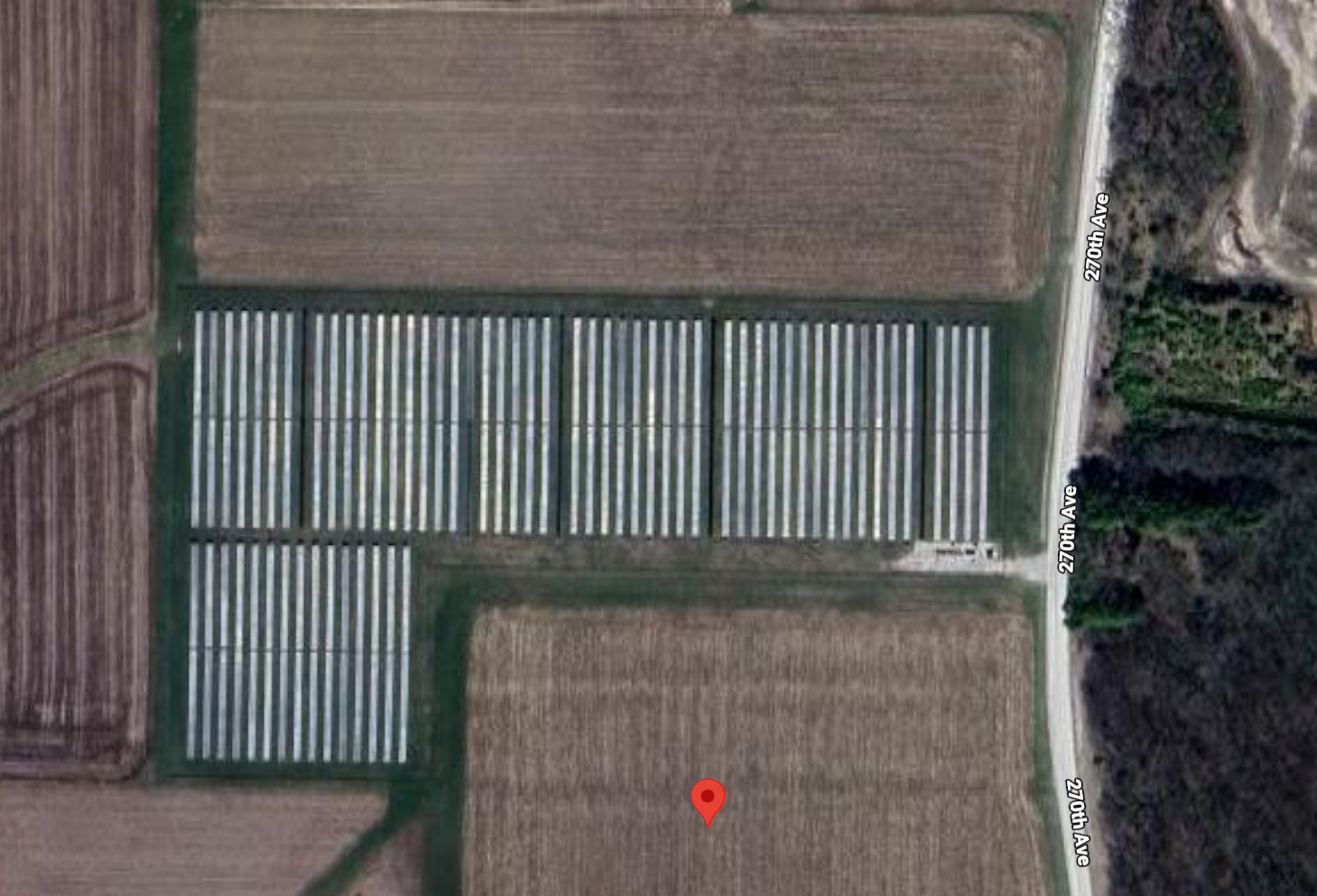 Agricultural field with a solar panel array, surrounded by other farmland.