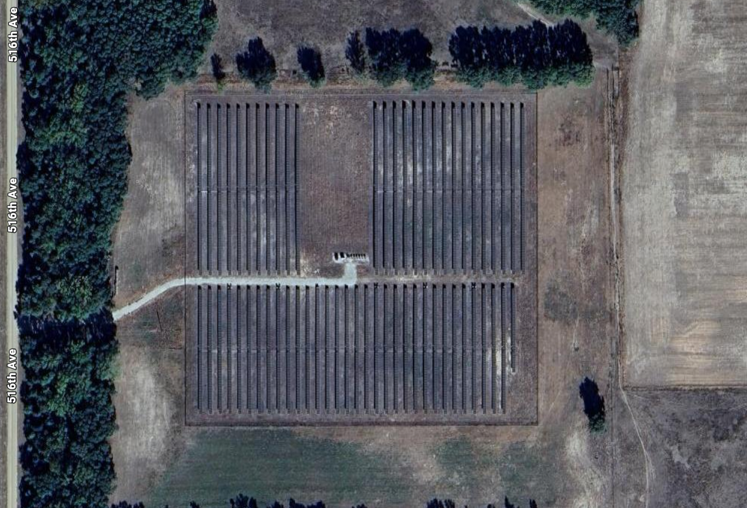 A large rectangular field with a solar farm, surrounded by trees and other fields.