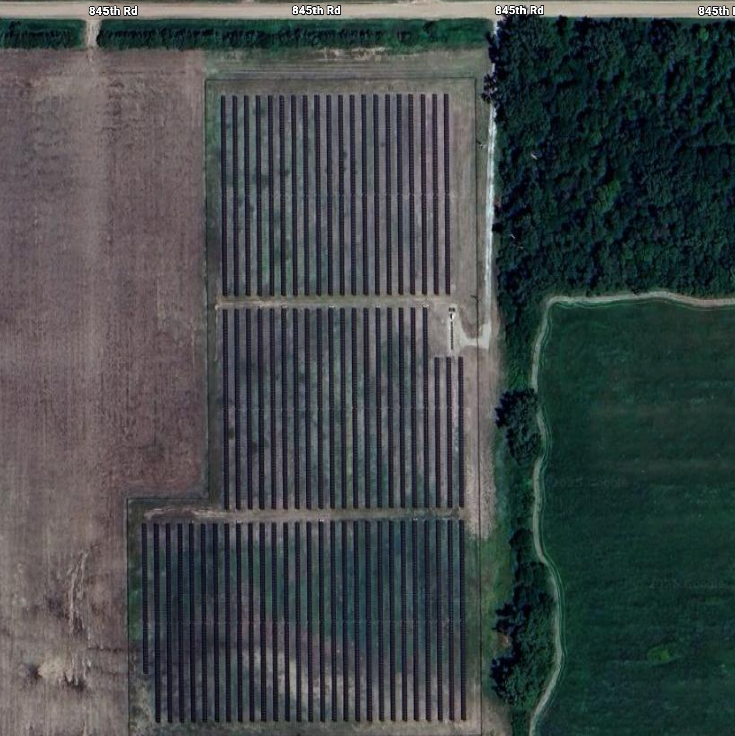 Aerial view of solar panels arranged in rows next to a green field.