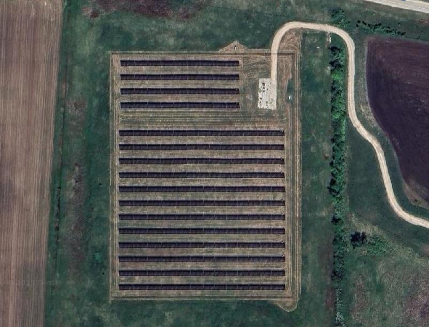 A large rectangular agricultural field of solar panels, surrounded by roads and greenery.