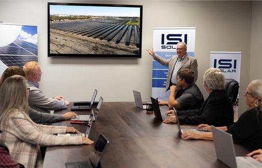 Meeting room with people around a table, discussing solar panels displayed on a screen.