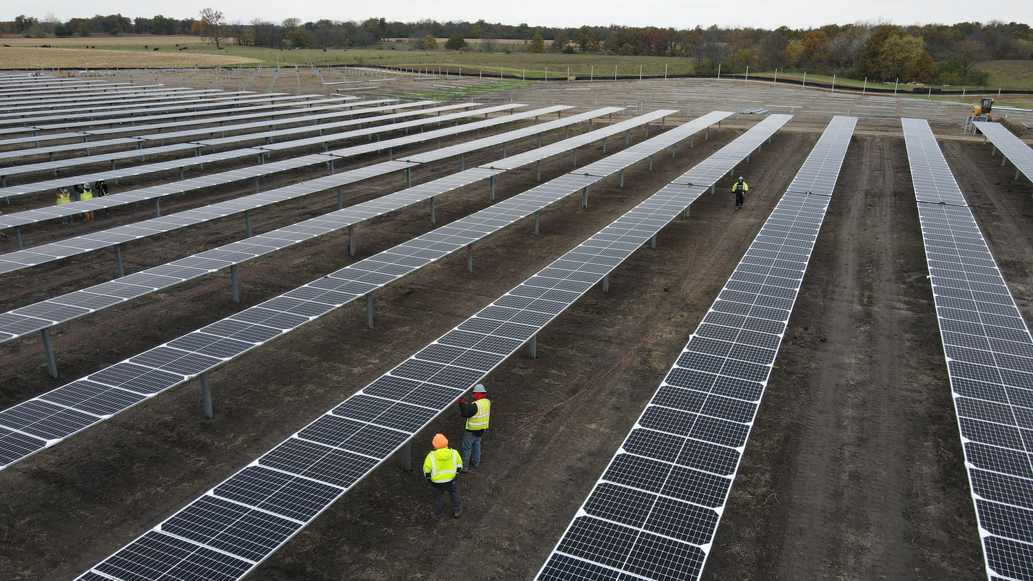 Solar panel installation site with workers in a field of solar panels.