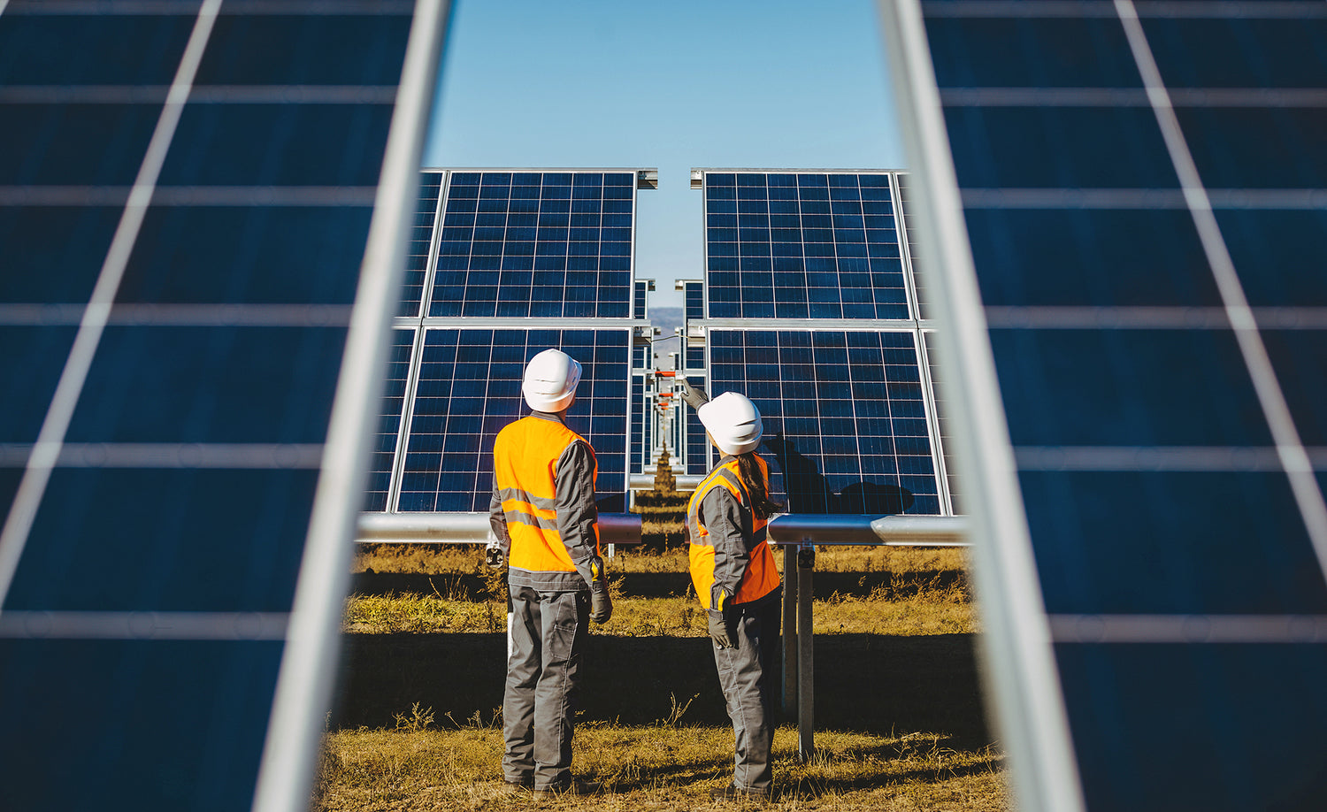 Two workers in high-visibility vests and hard hats inspecting solar panels.