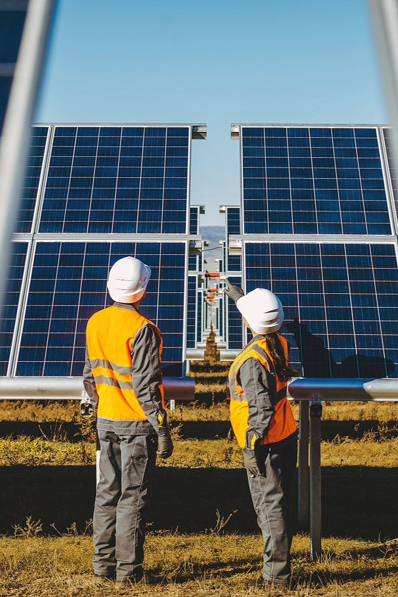 Two workers in high-visibility vests and hard hats inspecting solar panels on a clear day.