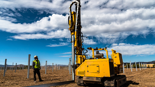 Yellow drilling machine on a construction site with a person in safety gear observing.