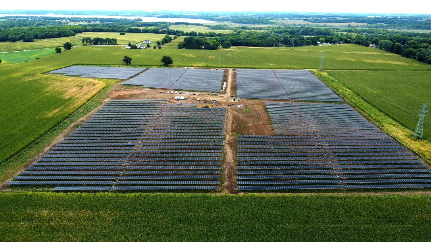 Bright green grass surrounds this solar panel site.  There are several cars parked in the middle of the solar panels, but they look small compared to the vast landscape. 